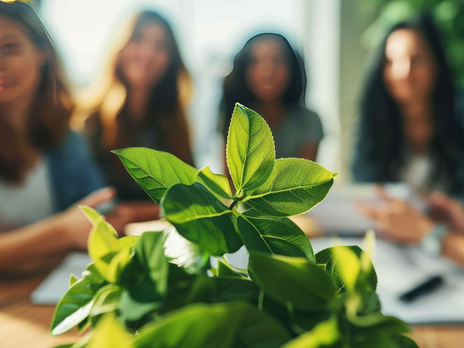 Gruppe von fünf Personen im Hintergrund, im Vordergrund frische grüne Blätter auf einem Tisch